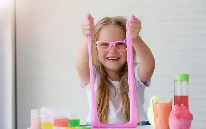 Een lachend meisje met roze bril speelt met roze slijm tijdens een wetenschappelijk experiment.