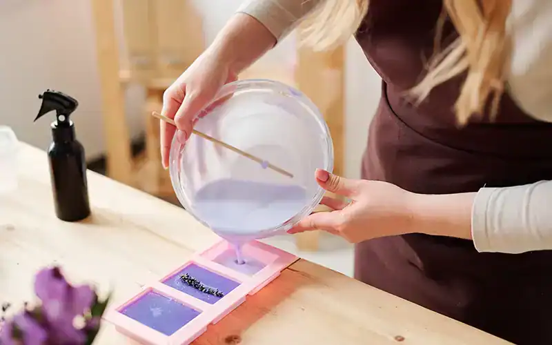 Een persoon giet paars zeepmengsel in siliconen zeepvormen.