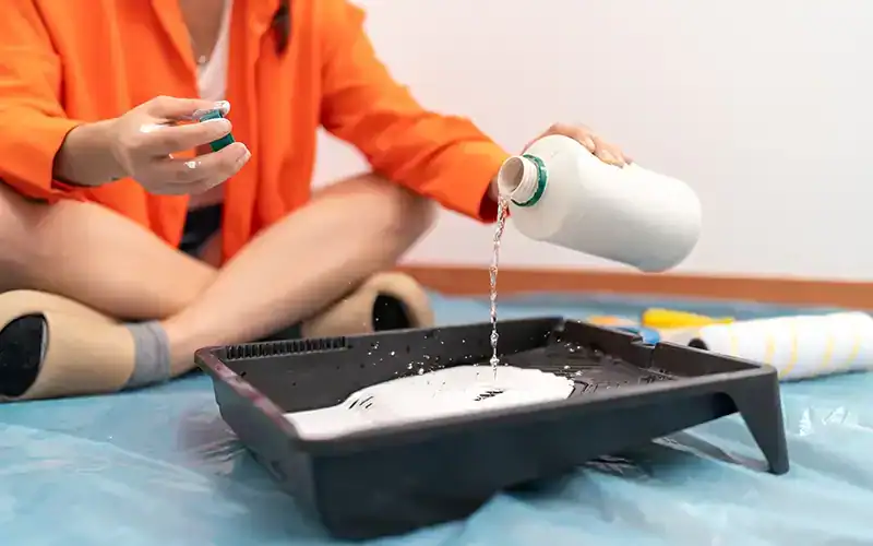 Persoon die vloeistof toevoegt aan verf in een verfbak om de verf te verdunnen.