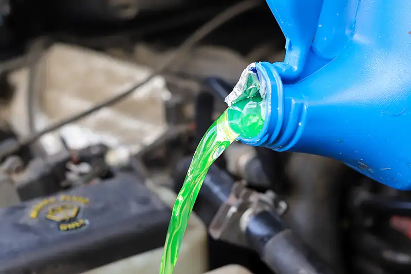 Frostschutzmittel wird aus einer Flasche in das Kühlsystem eines Autos gegossen.
