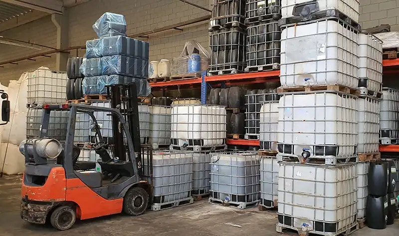 Bei diesem Chemikaliengroßhändler hebt ein Gabelstapler gestapelte Intermediate Bulk Container (IBCs) in einem Industrielager – ein typischer Anblick in der chemischen Industrie.