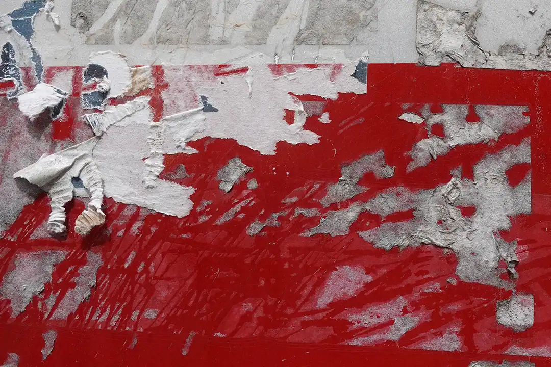 Eine Nahaufnahme hartnäckiger Klebereste auf einer roten Oberfläche mit teilweise abgerissenen und verblassten Papier- und Klebstoffschichten.