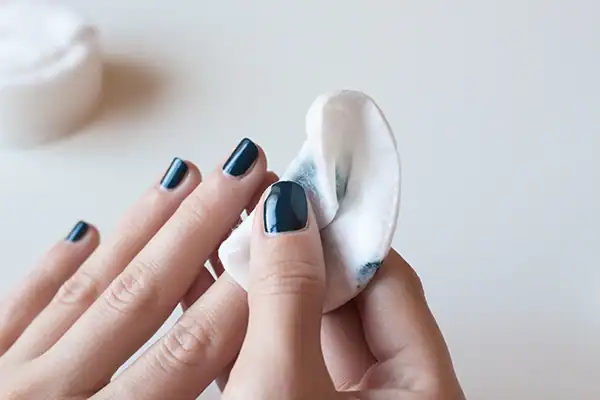 Eine Person entfernt mit Nagellackentferner vorsichtig den Lack von einer gepflegten Maniküre.