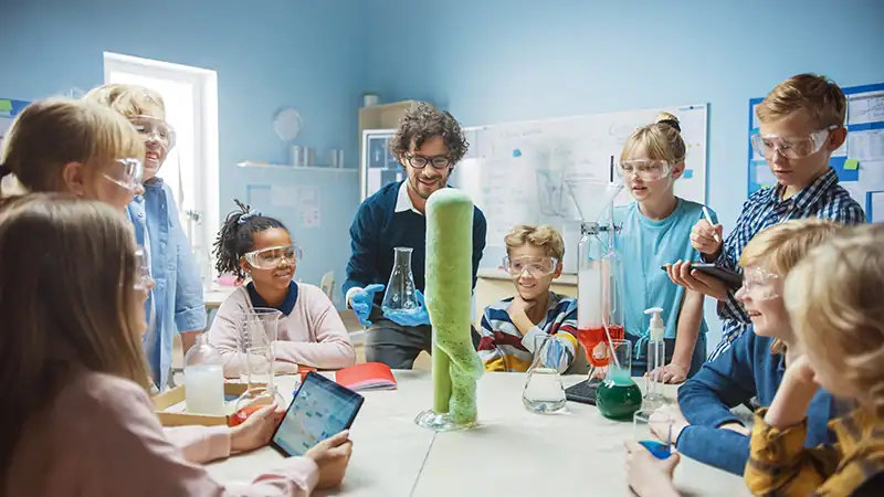 Kinder tragen Schutzbrillen und beobachten im Klassenzimmer eine Vorführung des Elefantenzahnpasta-Experiments.